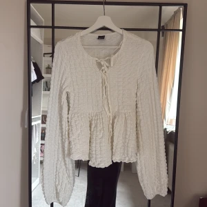 Vit blus med knyt och volang - Supersöt vit blus från Gina tricot med struktur i tyget, långa ärmar och knytning framtill. Blusen har volang nedtill. Perfekt för dig som gillar romantisk och trendig stil.