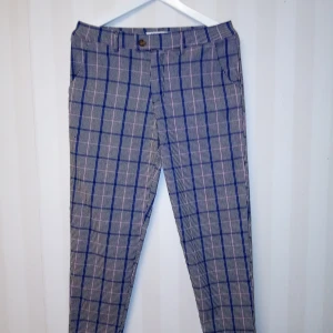 Rutig byxa från Frilivin, blå/rosa, M - Snygga byxor från Frilivin i rutig design med blå och rosa rutor på svartvit botten. Byxorna har normal passform, knäppning med två knappar och är tillverkade i en mix av viskos, nylon och elastan. Perfekta för dig som vill sticka ut med stil. Kan skickas med extra pris via post.
