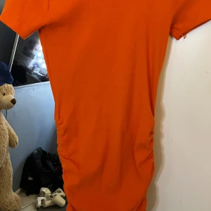 Orange kortärmad klänning - Snygg orange klänning med korta ärmar och enkel, rak passform. Klänningen har lätt rynkade sidor som ger en cool detalj och är perfekt för dig som gillar färg. Passar lika bra till sneakers som till boots.