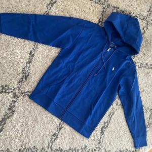Blå hoodie från Polo Ralph Lauren - Snygg blå hoodie från Polo Ralph Lauren med dragkedja och huva. Klassisk logga broderad på bröstet och praktiska fickor framtill. Perfekt för en chill och sportig look. Tillverkad i mjuk bomull för extra komfort. Storlek M passar även S. För frågor som måttet skriv PM.