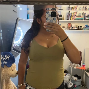 Olivgrön linnetopp med smala axelband - Snygg olivgrön linnetopp med smala axelband och v-ringad halsringning. Toppen är figurnära och har en enkel, stilren design som passar perfekt till jeans eller kjol. Perfekt för varma dagar och enkel att matcha med olika accessoarer.