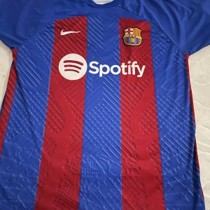 FC Barcelona Lewandowski matchtröja - Säljer en officiell FC Barcelona fotbollströja från Nike med Lewandowski och nummer 9 på ryggen. Tröjan har klassiska blå och röda ränder, klubbmärke på bröstet och Spotify som sponsor. Tillverkad i lätt och ventilerande material, perfekt för match eller träning.
