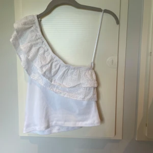 Vit oneshoulder topp med volang - Superfin vit oneshoulder topp från Gina Tricot med smalt axelband och bred volang med broderade blommor. Den är ifrån Gina Tricot Young i storlek 170 men sitter som XS🌺