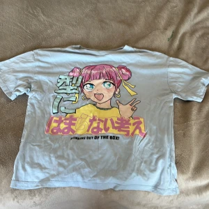 Ljusblå anime t-shirt från Zara - Ljusblå t-shirt från Zara med stor animeinspirerad print på framsidan i pastellfärger och japansk text. Motivet har rosa hår, gula detaljer och texten 'Thinking out of the box!'. Klassisk passform och rund hals. Perfekt för dig som gillar streetstyle och coola prints.
