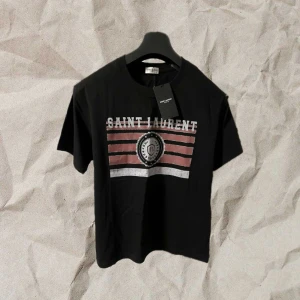 Saint Laurent T shirt - Säljer en svart Saint Laurent t-shirt i helt nytt skick. Aldrig använd. Snygg passform och enkel design med skön logga. Perfekt till både vardags och fest. Hojta till ifall du har frågor/funderingar🙌 den är ute för 749kr, men ifall du börjar följa mig kan jag släppa den för 699kr prick