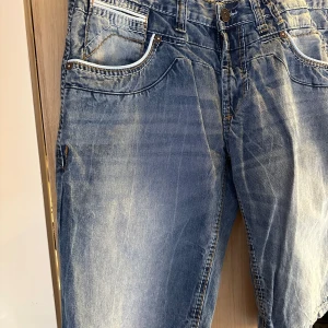 Blå jeanchorts  från SMOG i storlek L - Säljer ett par klassiska blå jeansshorts från SMOG i storlek L. Jeansen har en snygg tvättad look med ljusa partier, fem fickor och kontrastsömmar. De är raka i modellen och har normal passform. Perfekta för en avslappnad stil.