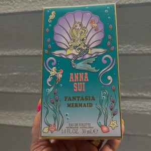 Anna Sui Fantasia Mermaid parfym - Parfymen Anna Sui Fantasia Mermaid i en färgglad ask med havstema, sjöjungfru, snäckskal och sjöhästar. Flaskan innehåller 30 ml eau de toilette och har en lekfull, drömsk design med turkosa, lila och guldiga detaljer.