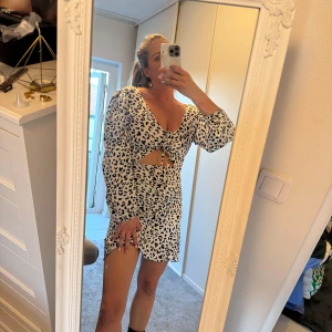 Leopardmönstrad kort klänning med cut-out - Snygg kort klänning med svartvitt leopardmönster, v-ringning och långa puffärmar. Klänningen har cut-out detalj under bysten och knyt framtill. Materialet känns lätt och flowy. 