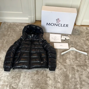 Marine blå Moncler dunjacka med huva - Säljer en marine blå, glansig dunjacka från Moncler med huva och dragkedja. Jackan har Moncler-logga på ärmen, två fickor med dragkedja och quiltad design. Perfekt för kalla dagar och riktigt snygg streetstil. Fodret är i dun och yttermaterialet är syntet. Box,galge, extra knappar och ett tack kort med kommer💚Kvitto kan visas vid förfrågan✅👋