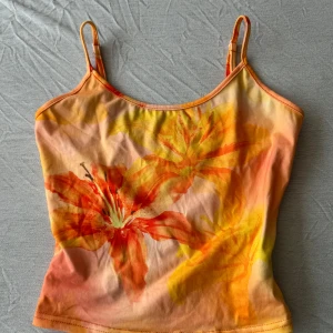 Blommig linnetopp från SHEIN XS - Snygg linnetopp från SHEIN i storlek XS med tunna axelband och blommigt mönster i orange, gul och röd. Toppen har en somrig vibe med stora blommor framtill och justerbara band. Perfekt för varma dagar och att styla med jeans eller kjol.