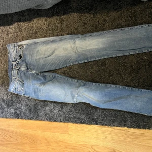 Replay Hyperflex ljusblå jeans - Säljer ett par ljusblå Replay Hyperflex jeans med klassisk femficksdesign och snygga slitningar. Jeansen har smal passform och är tillverkade i stretchigt denim för extra komfort. Perfekta för dig som gillar en avslappnad men ändå stilren look.