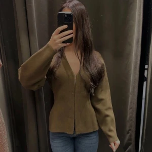 Olivgrön v-ringad kofta - Snygg olivgrön kofta med v-ringning och vida ärmar. Tröjan har en figurnära passform upptill och faller snyggt över höfterna. Perfekt att styla med jeans eller kjol för en trendig look. Passar mig som vanligtvis brukar ha storlek xs