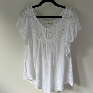 Vit blus med broderad spets Hollister - Superfin vit blus från Hollister med broderad spets upptill och liten knappdetalj vid halsen. Luftig och sval topp, perfekt till sommarn.     Tryck gärna på köp nu!❣️