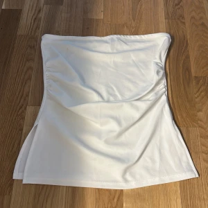 Vit bandeau tubtopp - Snygg vit bandeau tubtopp med enkel och clean design. Toppen är ärmlös och har en lätt stretchig passform som sitter skönt mot kroppen. Perfekt att styla med jeans eller kjol för en fräsch look.
