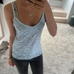 Ljusblå spetslinne med smala axelband - Supersött ljusblått linne i spets med smala axelband och v-ringning. Hela toppen är täckt av blommigt spetsmönster som ger en romantisk vibe. Perfekt att styla lager på lager eller som den är under varma dagar.Knappt använd.