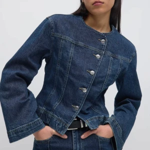 Mörkblå jeansjacka med raka ärmar - Snygg mörkblå jeansjacka med raka, vida ärmar och markerad midja. Jackan har rund halsringning och knäpps med silverfärgade knappar framtill. Perfekt för dig som gillar en clean och stilren denimlook. Säljer då den inte kommer till användning❣️