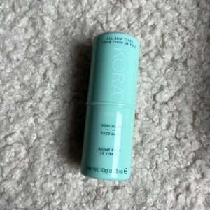 KORA Organics Noni Glow Face Balm - Glow face balm från KORA Organics i en smidig mintgrön stick-förpackning. Balsamet är genomskinligt och passar alla hudtyper. Perfekt att använda för extra lyster och återfuktning i ansiktet. Innehåller 10g och är enkel att ta med i väskan.