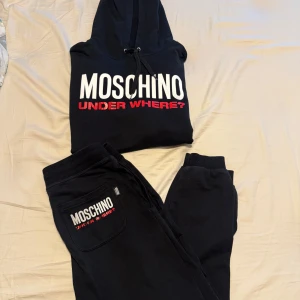 Svarta mjukisbyxor från Moschino - Svarta mjukisbyxor från Moschino med broderad logga i vitt och rött på bakfickan. Byxorna har resår och snörning i midjan samt muddar vid bensluten. Tillverkade i mjukt bomullsmaterial för maximal komfort.