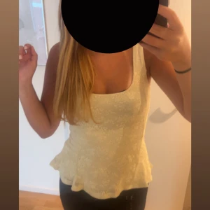 Ljusgul spetsig linnetopp - Supersöt ljusgul linnetopp med blommigt spetsmönster och lätt utsvängd nederkant. Toppen är ärmlös med breda axelband och har en feminin, romantisk vibe. Endast använt 1 gång! 
