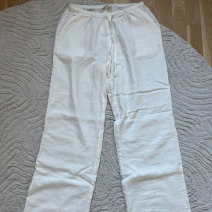 Vita linnebyxor från Madlady - Säljer ett par supersnygga vita linnebyxor från Madlady i Storlek S-regular. Byxorna är luftiga och har elastisk midja med snörning, raka ben och sidfickor. Materialet är linne som ger en fräsch och luftig känsla under varma dagar.