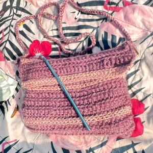 Handgjord lila stickad axelväska - Säljer en unik, handgjord axelväska i lila och ljusrosa toner. Väskan är stickad med grovt garn och har ett långt axelband. Perfekt för dig som vill ha något personligt och mysigt. Rymmer mobil, plånbok och småprylar. Superfin detalj till din outfit!