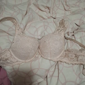 Beige spetsig korsett-topp - Säljer en beige korsett-topp med vacker spets och vadderade kupor. Toppen har fina spetsdetaljer över hela framsidan och längs banden, vilket ger en romantisk och feminin look. Perfekt för att styla lager på lager eller som statement-piece.