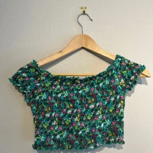 Grön blommig croppad topp - Superfin kort sommartopp med grönblommigt mönster. Kan bäras på axlarna eller off-shoulder. Jag tror att den är från H&M men är inte helt säker då lappen är bortklippt