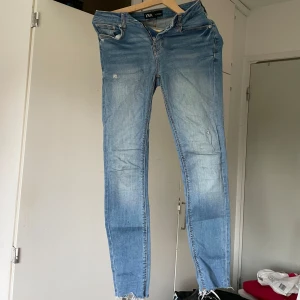 Ljusblå skinny jeans från Zara - Säljer ett par ljusblå skinny jeans från Zara med slitna detaljer och råa kanter vid bensluten. Jeansen har klassisk femficksdesign, dragkedjegylf och är tillverkade i stretchig bomullsdenim för en tight passform.
