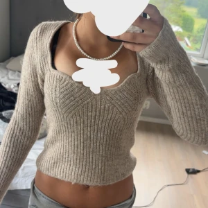 Beige ribbad stickad tröja - Superfin beige stickad tröja med ribbad struktur och snygg sweetheart-urringning. Modellen är croppad och har långa ärmar, perfekt för lager-på-lager. Passar dig som gillar en enkel men trendig look.