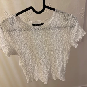 Vit topp - Superfin vit topp från Gina Tricot med crinklad struktur och korta ärmar. Modellen är croppad och har en lätt vågig kant nertill och vid ärmslut. 
