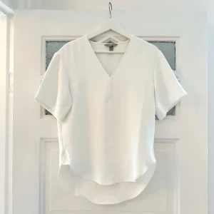 Vit v-ringad blus från H&M - Oanvänd vit blus. Tjockare fint material som faller snyggt och man inte ser igenom. Storlek XS men oversized modell så passar mig som har S, kanske även liten M. Aldrig använd, endast prislapp borttagen.