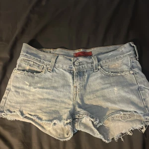 Levi's ljusblå jeansshorts med fransar - Ljusblå jeansshorts från Levi's med råa, fransiga kanter och slitna detaljer. Perfekta för en avslappnad och cool stil under varma dagar.