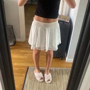 Vit kortkjol med smock i midjan - Supersöt vit kortkjol med flowig känsla och bred smock i midjan. Kjolen har ett tunt, lätt tyg som ger ett luftigt fall och passar perfekt till varma dagar. Enkel att matcha med crop tops eller stickade tröjor för en chill look. Den är från början en avklippt klänning så varken märke eller storlek finns kvar. Dock vet jag att den är från chelsea och borde vara runt storlek XS💗