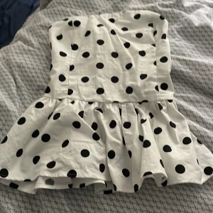 Prickig volangtopp från Bik Bok - Supersöt vit topp med svarta prickar från Bik Bok. Modellen är axelbandslös med volang nertill och smockad rygg för extra komfort. Perfekt för dig som gillar en lekfull och trendig stil. Toppens material känns lätt och luftig, perfekt för varma dagar. Alldrog använd, lappen kvar.