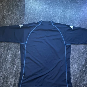 Mörkblå kortärmad tröja från Kappa - Sportig mörkblå kortärmad tröja från Kappa med blå kontrastsömmar och broderad Kappa-logga på ärmarna. Tillverkad i mjukt och stretchigt polyestermaterial, perfekt för träning eller chill. Snygg och enkel design med rund hals.