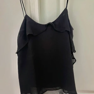 Svart volang-linnetopp från Mango - Svart linnetopp från Mango med tunna axelband och snygga volangdetaljer längs sidorna och upptill. Toppens material är lätt och luftigt. Skriv om ni har frågor! :)