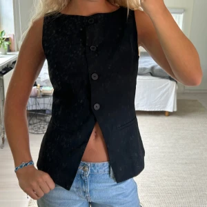 Svart klassisk väst med knappar - Snygg svart väst med rak passform och fyra knappar framtill. Västen har två fejkade fickor och en stilren, enkel design som passar till jeans eller kjol. 