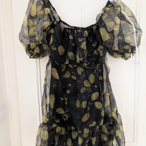 Blommig klänning från missguided  - Svart klänning med citroner på i storlek 34. Inköpt från missguided. Helt ny med prislappen kvar. Den svarta inne klänningen sitter inte ihop med över klänningen. De två går alltså att separera