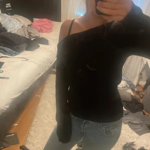 Svart offshoulder stickad tröja - Säljer en svart stickad tröja med offshoulder-design. Tröjan har lång ärm och en loose passform som ger en avslappnad och trendig look. Perfekt att styla med jeans för en cool vardagsoutfit.