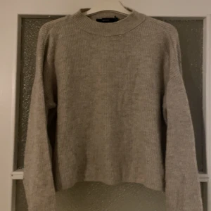 Beige stickad tröja med rund hals - Mysig beige stickad tröja med rund hals och långa ärmar. Tröjan har en enkel och stilren design med ribbad struktur, perfekt för lager-på-lager och chill dagar.