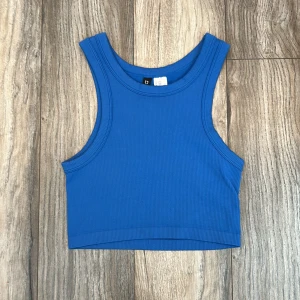 Blå ribbad linnetopp från H&M Divided - Snygg blå croppad linnetopp från H&M Divided i ribbad bomullskvalitet. Modellen är ärmlös med breda axelband och rund halsringning. Använd gärna Early Bird som fraktalternativ.