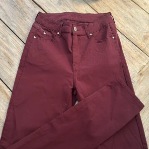 Vinröda byxor Casual Wear Kelly 36N - Snygga vinröda byxor från Casual Wear, modell Kelly. Klassisk femficksdesign med raka ben och normal passform. Tillverkade i en mjuk mix av viskos, polyester och elastan för skön stretch. Perfekta för dig som vill ha en stilren look med lite edge.