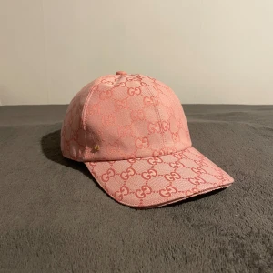 Gucci Dubai keps rosa - Snygg rosa keps från Gucci med ikoniskt GG-mönster över hela kepsen. Justerbar rem baktill för perfekt passform. Tillverkad i bomull med klassisk böjd skärm och broderad logga. Perfekt accessoar för att lyfta din outfit.