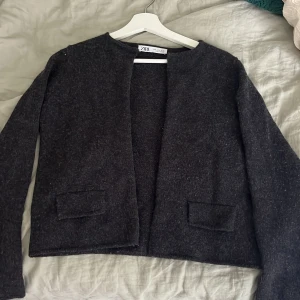 Mörkgrå ullkofta från Zara, S - Mysig mörkgrå jacka från Zara i ullmix med rak passform och lång ärm. Enkel, stilren design utan krage och med två fickor framtill. Kan även knäppas med en knapp längst upp. Perfekt för lager-på-lager och funkar till många olika outfits. Använd fåtal gånger.