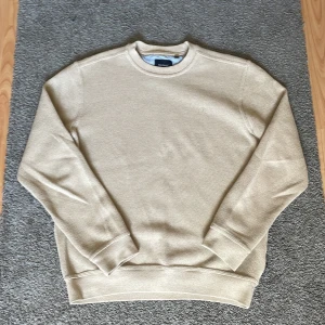 Beige stickad tröja från Sea Ranch - Snygg beige stickad tröja från Sea Ranch i storlek M. Tröjan har rund halsringning, diskret broderad logga på bröstet och ribbade muddar vid ärmslut och nederkant. Perfekt för lager-på-lager och chill stil.