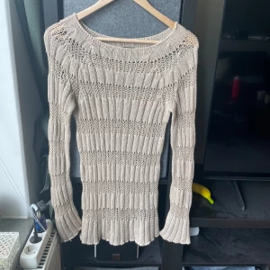 Beige stickad tröja från Motivi - Säljer en beige stickad tröja från Motivi, tillverkad i Italien. Tröjan har lång ärm, ribbade detaljer och ett luftigt stickmönster. Perfekt för lager-på-lager och passar till många olika stilar.