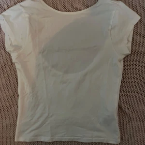 Vit topp med djup urringning från Gina Tricot - Säljer en enkel och stilren vit topp från Gina Tricot. Toppen har korta ärmar och en djup, rund urringning framtill. Perfekt att matcha med jeans eller kjol för en clean look.