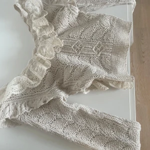 Beige stickad tröja med spetsvolang - Supersöt beige stickad tröja med bred volang i spets längs halsringningen och axlarna. Har en liten fläck på framsidan