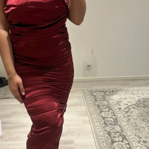 Vinröd långklänning från Girlcode - Säljer en vinröd långklänning från Girlcode i glansigt material. Klänningen har tight passform och är ärmlös med lätt rynkade detaljer längs sidorna. 