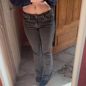 Grå bootcut jeans - Säljer ett par grå jeans med bootcut passform och klassiska fem fickor. Jeansen har låg midja och svarta sömmar, samt snygga detaljer på bakfickorna. Perfekta för dig som gillar en tidlös stil.